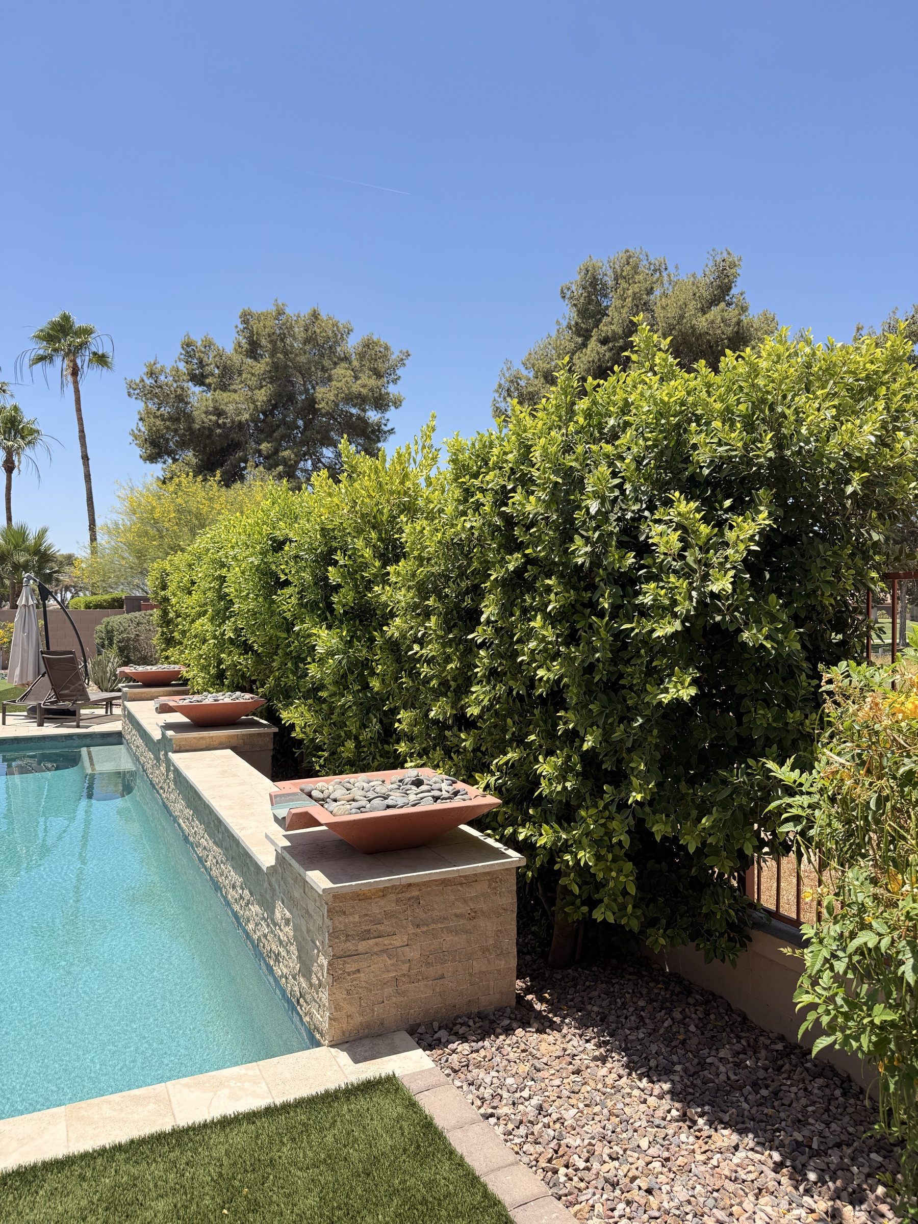 Copper fire bowls atop stacked stone pool wall with manicured ficus hedge
